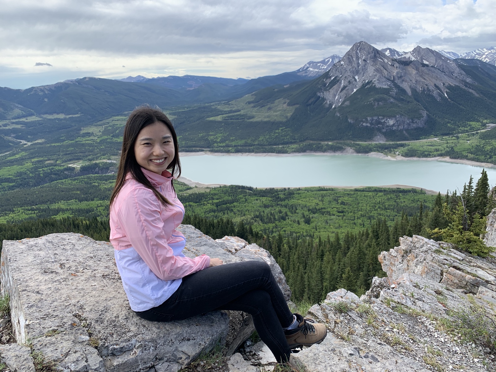 Boram smiling on a mountain summit overlooking a lake and forest